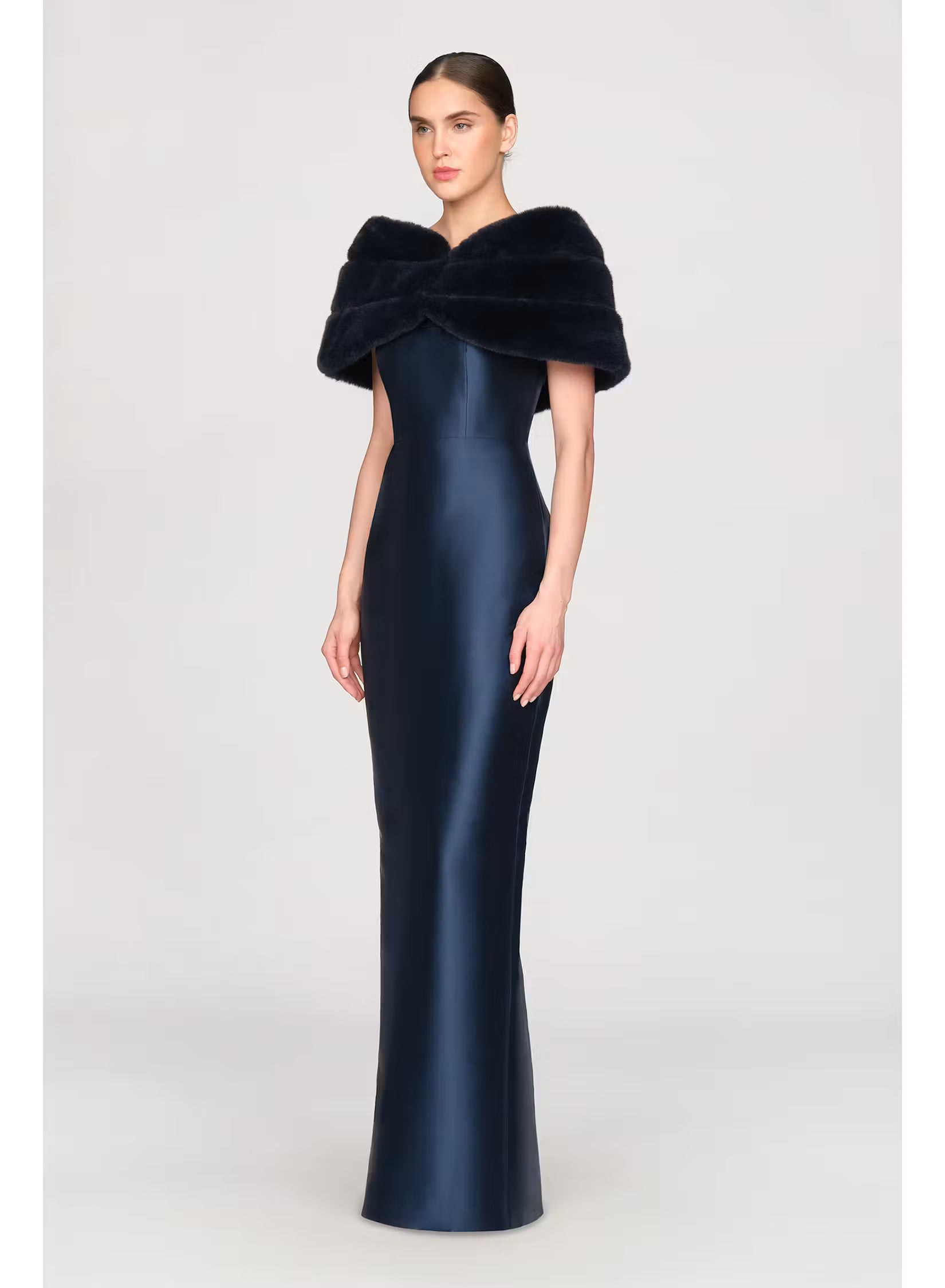 A model showcases a sleek, navy satin gown featuring a stylish faux mink shawl that elegantly wraps around the shoulders.