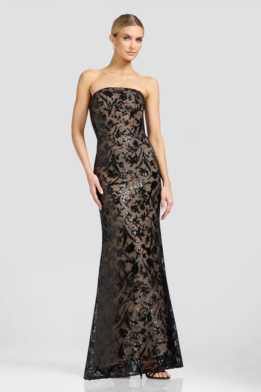 A model showcases a stunning strapless black gown adorned with intricate floral patterns and shimmering details, perfect for formal events like galas or black tie weddings.