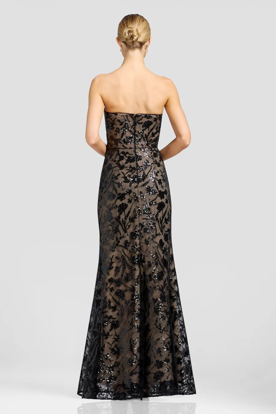 A woman is seen from the back, wearing a stunning strapless black gown adorned with floral metallic patterns and sequins.