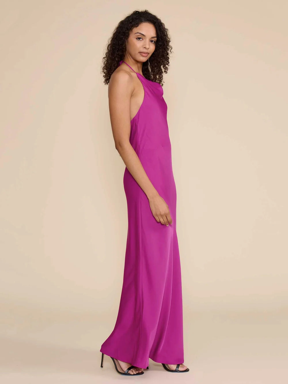 A model showcases a stunning magenta satin halter dress with a cowl neckline, perfect for elegant occasions like galas or black tie weddings. This eye-catching gown is conveniently available near Apex, Cary, and Raleigh.