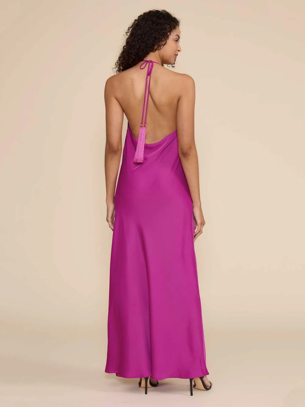A model showcases a stunning magenta halter dress with a cowl neckline and an open back, featuring elegant tassel details.