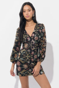 A model poses in a fitted mini dress featuring a deep V-neck and long, puffed sleeves adorned with vibrant floral embroidery against a black background.