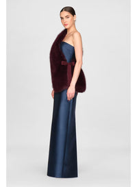 A model poses in profile wearing a sleek navy gown complemented by a rich burgundy faux fur stole. This elegant outfit is perfect for formal occasions such as galas or black tie weddings, conveniently available near Apex, Cary, and Raleigh.