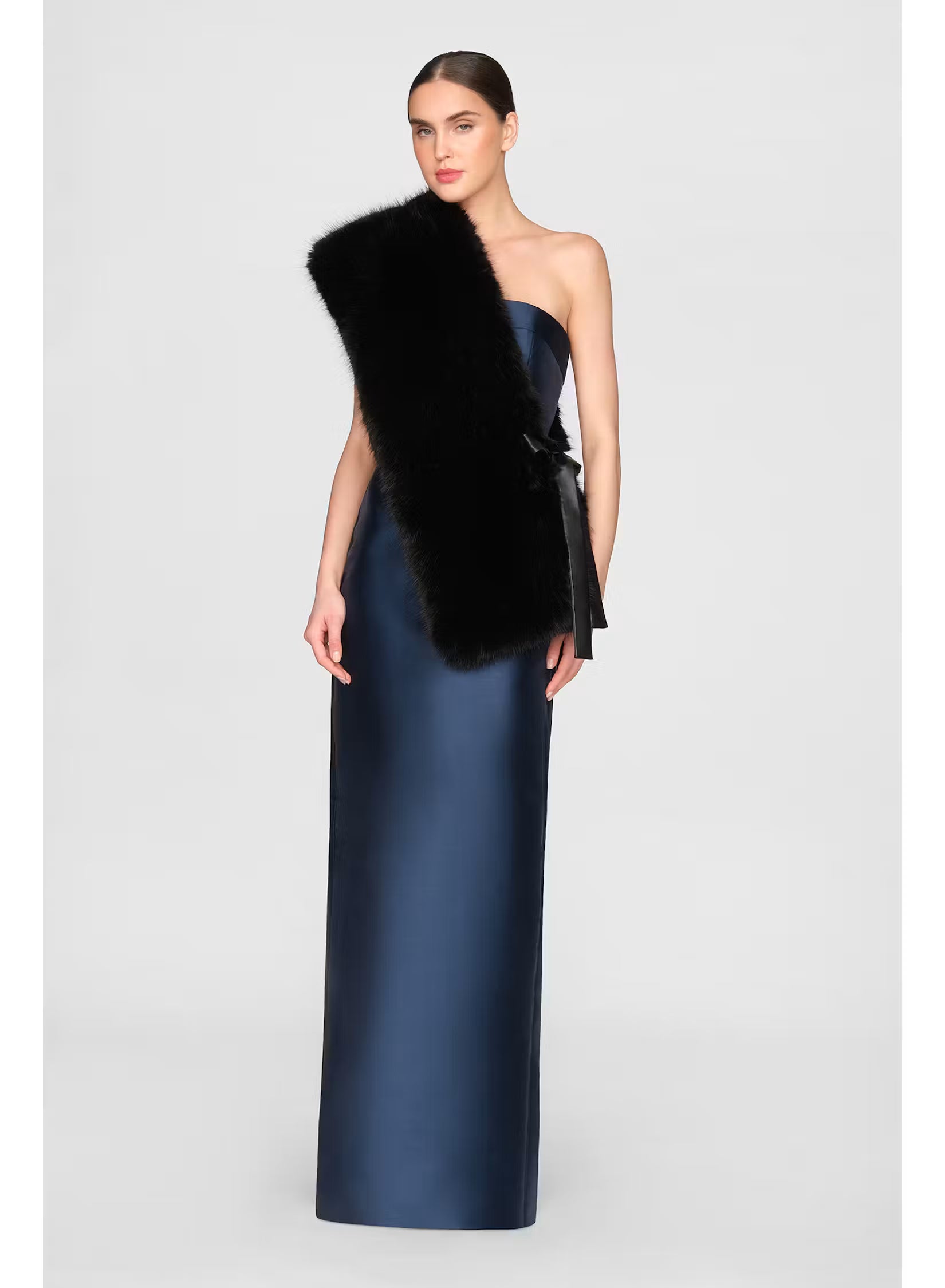 A model showcases a sleek, navy satin gown paired with a luxurious black faux fox stole draped over one shoulder.