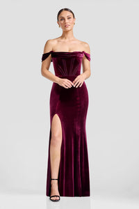 A model showcases a stunning off-the-shoulder mermaid gown in rich burgundy velvet, featuring a thigh-high slit and structured bodice.