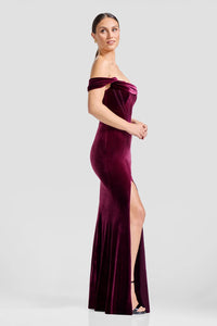 A model showcases a stunning off-the-shoulder dark chocolate gown with a mermaid silhouette and a high slit, perfect for a black tie wedding or gala. This elegant dress is conveniently located near Apex, Cary, and Raleigh.