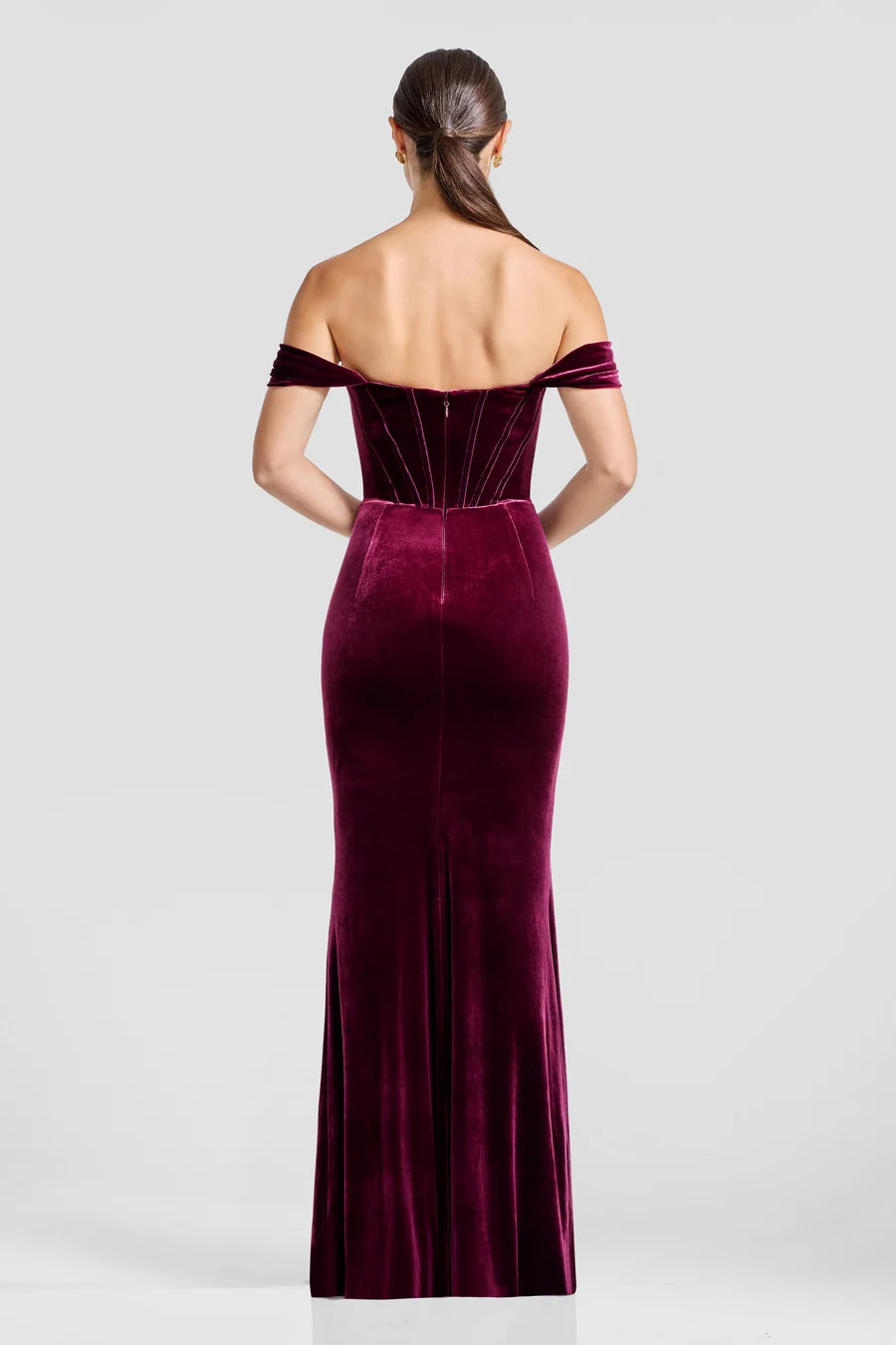A woman models a stunning off-the-shoulder gown in rich burgundy velvet, showcasing a fitted mermaid silhouette with a subtle slit.