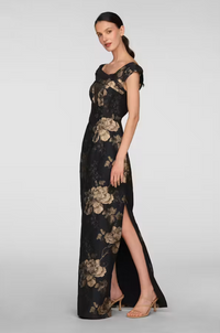 A model showcases an elegant black gown adorned with gold floral patterns and a thigh-high slit, ideal for formal events like galas or black-tie weddings. This stunning dress is conveniently available near Apex, Cary, and Raleigh.