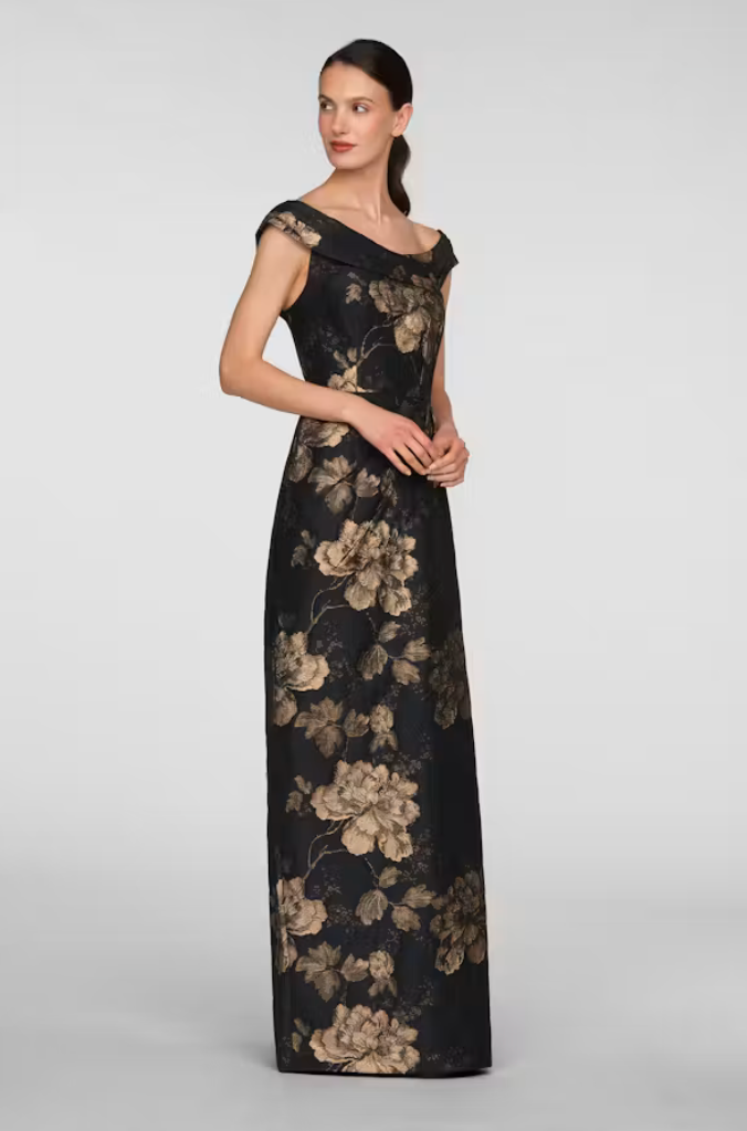 A model showcases an elegant black gown adorned with gold floral patterns, featuring an off-the-shoulder neckline.