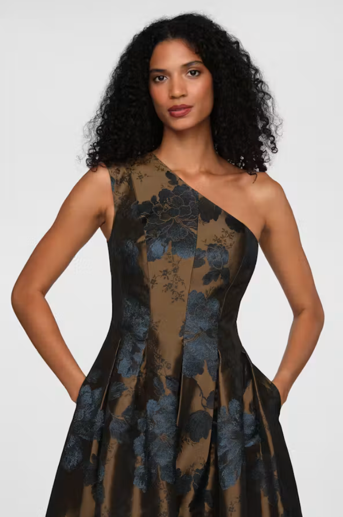A model showcases a stylish one-shoulder gown featuring a floral design in dark blue and brown tones. This elegant dress is perfect for formal events like galas or black tie weddings, and is conveniently available near Apex, Cary,.