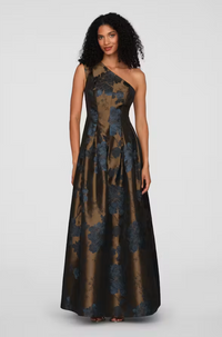 A model stands confidently in a stunning one-shoulder gown featuring a floral pattern in deep blue and gold hues.