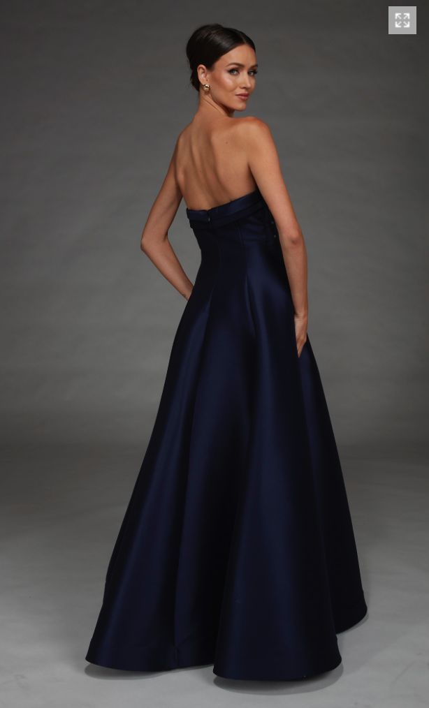 A model showcases a stunning strapless navy gown with a flowing skirt, ideal for elegant occasions like prom, gala events, or black tie weddings. This dress is conveniently located near Apex, Cary, and Raleigh for easy access.