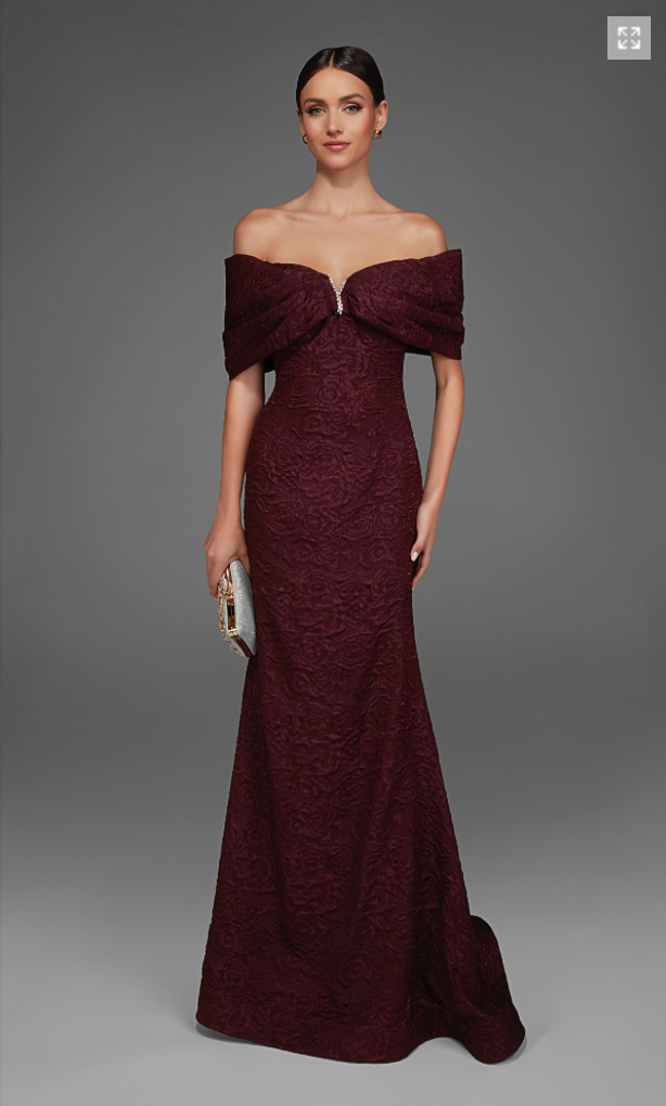 A model showcases an elegant off-the-shoulder gown in a rich black cherry hue, featuring intricate floral patterns and a fitted silhouette.