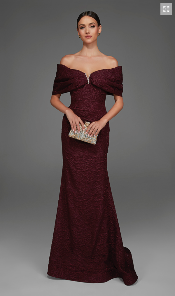 A model is showcasing an elegant off-the-shoulder burgundy gown with intricate floral detailing and a fitted silhouette.