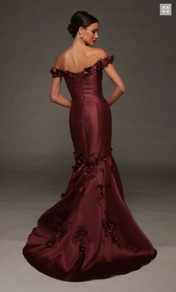 A model showcases a stunning burgundy gown with off-the-shoulder sleeves and floral embellishments, designed for elegant occasions like galas or formal weddings. This beautiful dress is conveniently available near Apex, Cary, and Raleigh.