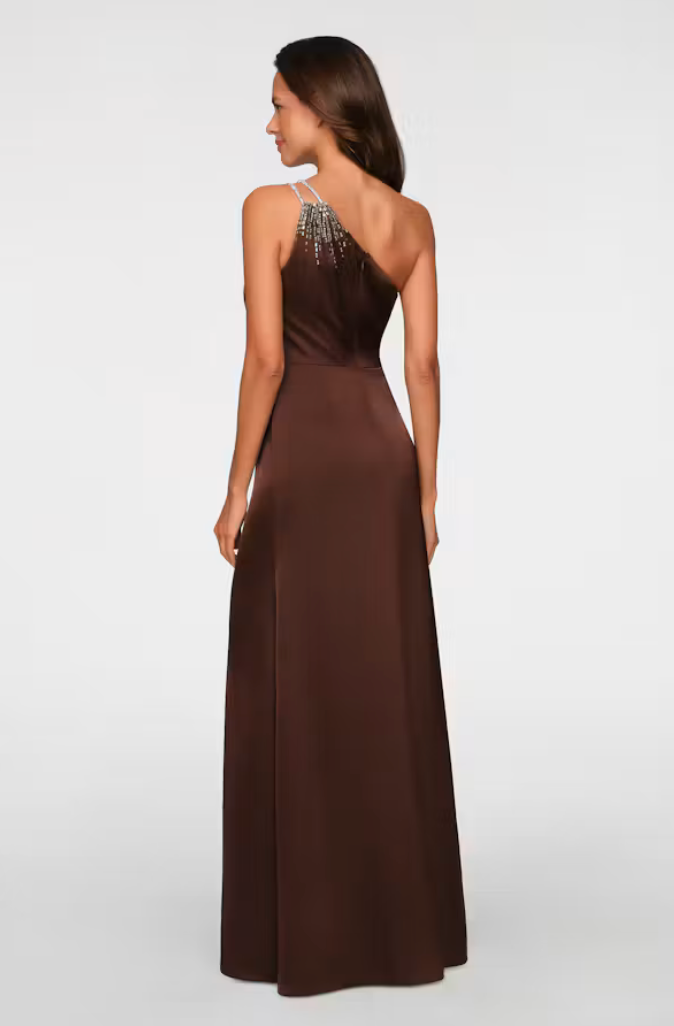 A model showcases a sleek brown one-shoulder gown featuring elegant embellishments on the shoulder. This stunning dress is perfect for formal occasions such as weddings, galas, or proms, and is available near Apex, Cary, and Raleigh.
