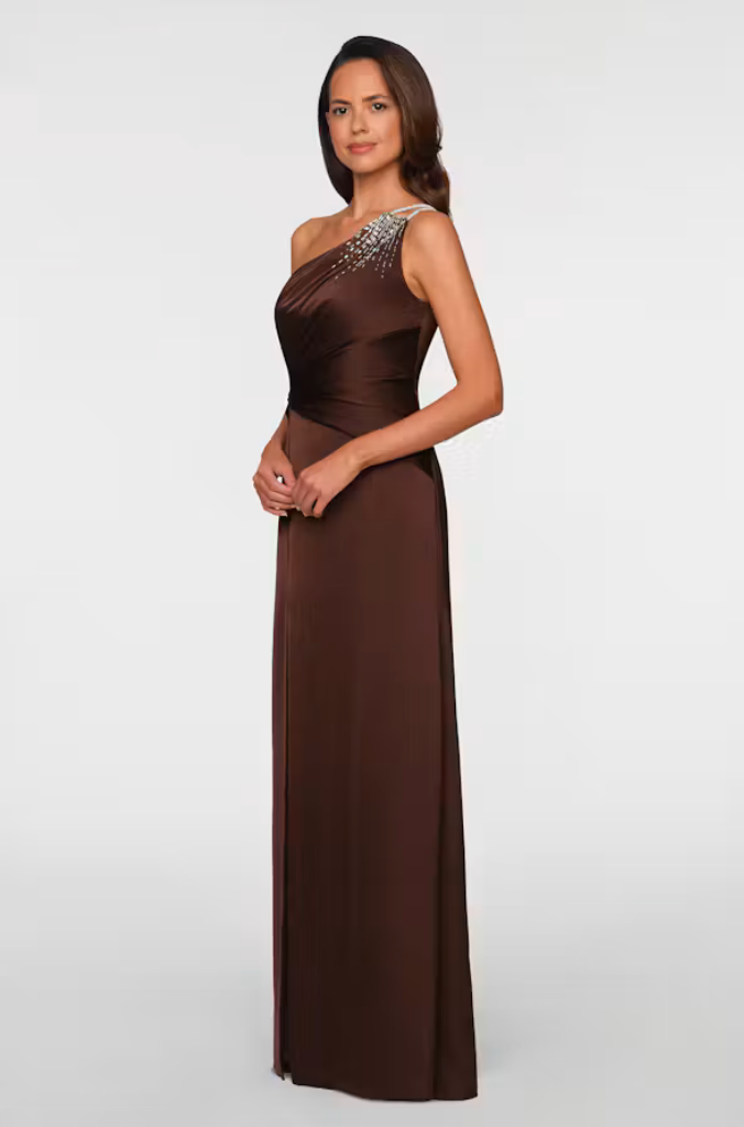 A model showcases a stylish brown one-shoulder gown featuring an elegant beaded detail on the shoulder. This versatile dress is perfect for formal occasions like weddings or galas, conveniently available near Apex, Cary, and Raleigh.