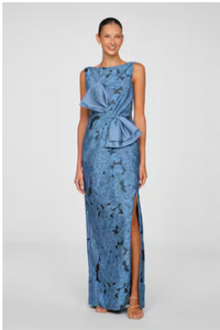 A model showcases a stunning blue gown featuring a large bow detail and a thigh-high slit, suitable for elegant occasions like a gala or black-tie wedding.