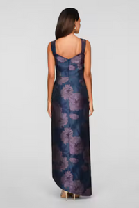A woman is wearing a stunning floral-patterned gown with a fitted bodice and flowing skirt, showcasing an elegant back design.