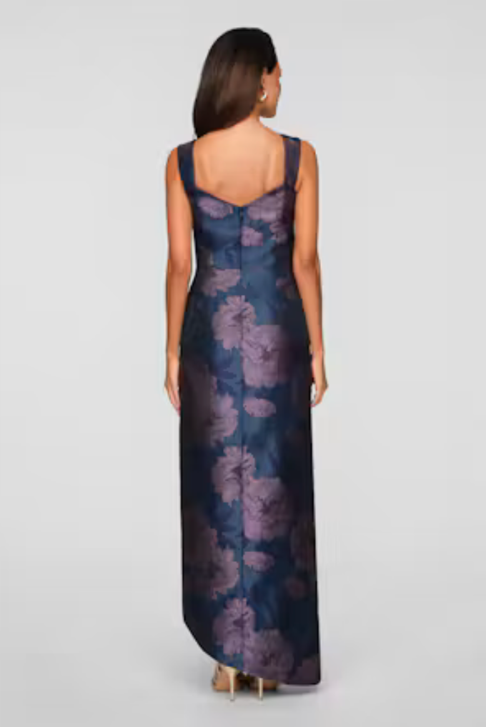 A woman is wearing a stunning floral-patterned gown with a fitted bodice and flowing skirt, showcasing an elegant back design.