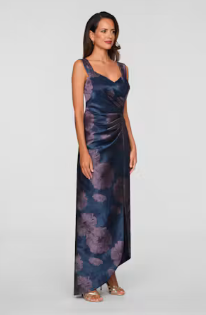 A model showcases a stunning navy gown with a floral pattern, featuring a draped design and a sleek silhouette. Ideal for elegant occasions like a black tie wedding or gala, this dress is conveniently available near Apex, Cary, and Raleigh.