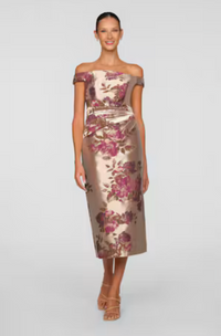 A woman models an elegant, off-the-shoulder tea-length dress adorned with a floral pattern in shades of pink and gold.