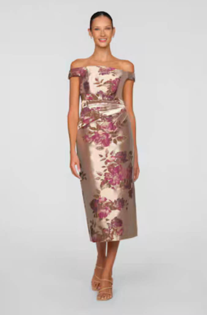 A woman models an elegant, off-the-shoulder tea-length dress adorned with a floral pattern in shades of pink and gold.
