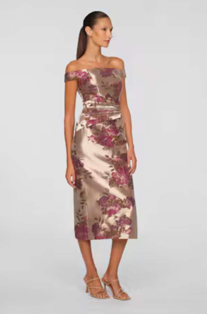 A woman models an elegant off-the-shoulder tea-length dress with a floral design in shades of burgundy and gold.