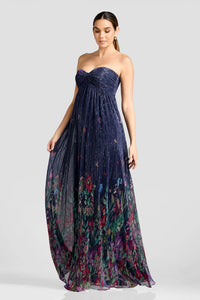 A model poses in a stunning strapless gown featuring a flowing floor-length skirt adorned with vibrant floral patterns. Perfect for special occasions like proms or galas, this dress is conveniently available near Apex, Cary, and Raleigh.