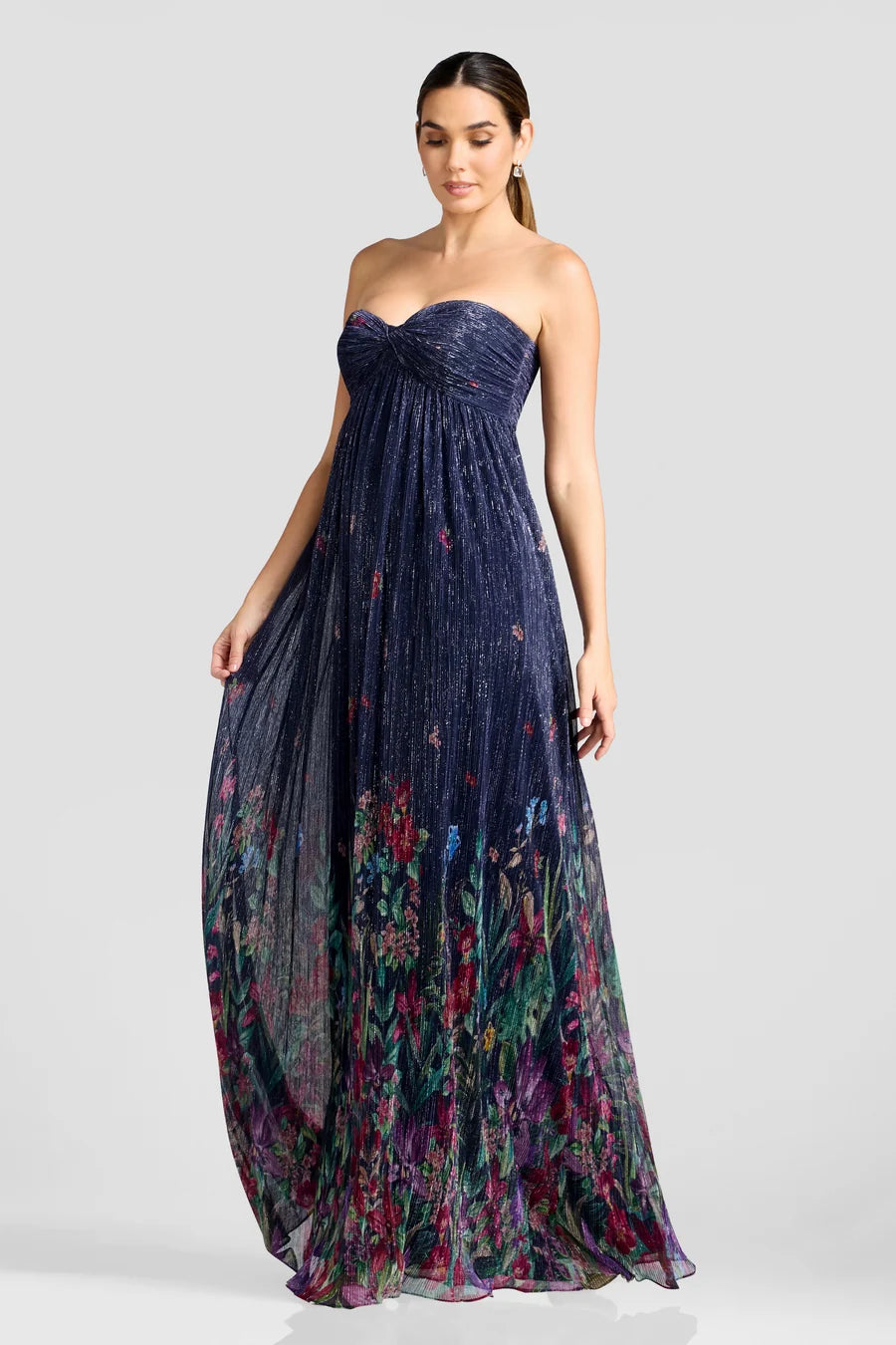 A model poses in a stunning strapless gown featuring a flowing floor-length skirt adorned with vibrant floral patterns. Perfect for special occasions like proms or galas, this dress is conveniently available near Apex, Cary, and Raleigh.