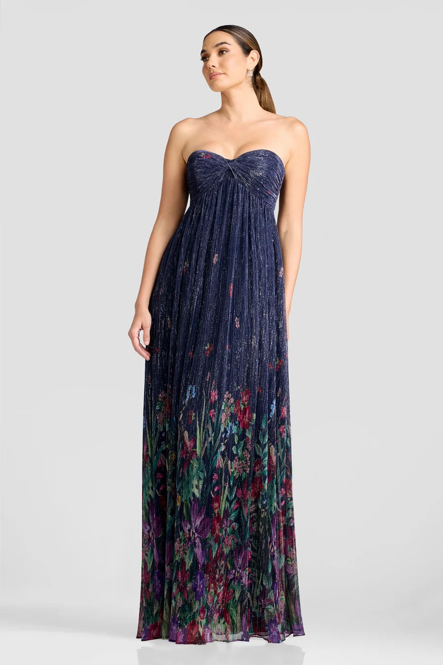A model showcases a stunning strapless gown with a shimmering floral design in deep navy and vibrant colors at the hem.