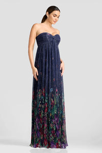 A model showcases a floor-length strapless gown featuring shimmering pleated fabric with a floral design in vibrant colors.