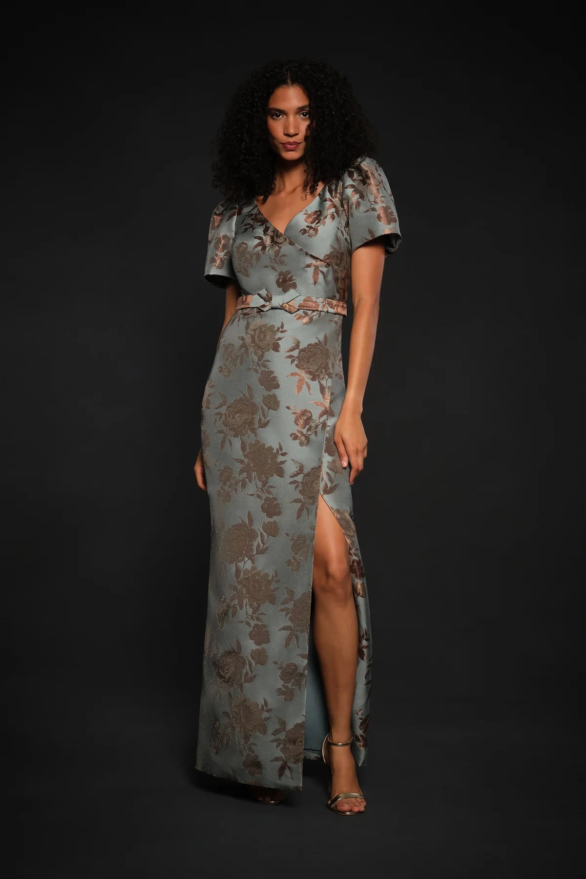 A model showcases a vintage floral jacquard gown in cool blue, featuring a faux-surplice bodice, short sleeves, and a front slit.
