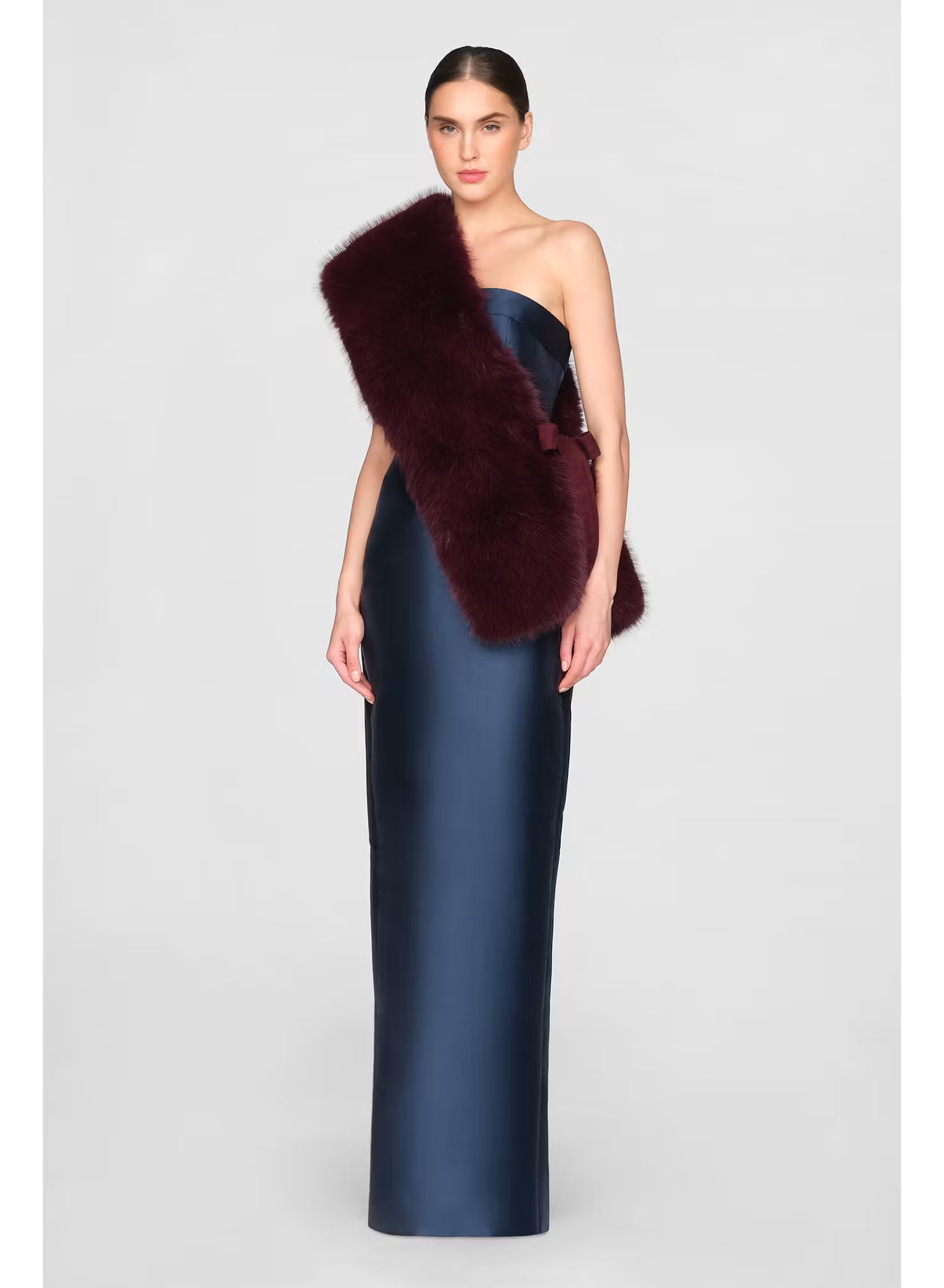 A model showcases a sleek navy gown paired with a luxurious faux fur stole in a rich burgundy hue. This elegant outfit is perfect for formal events such as galas or black tie weddings, conveniently located near Apex, Cary, and Raleigh.