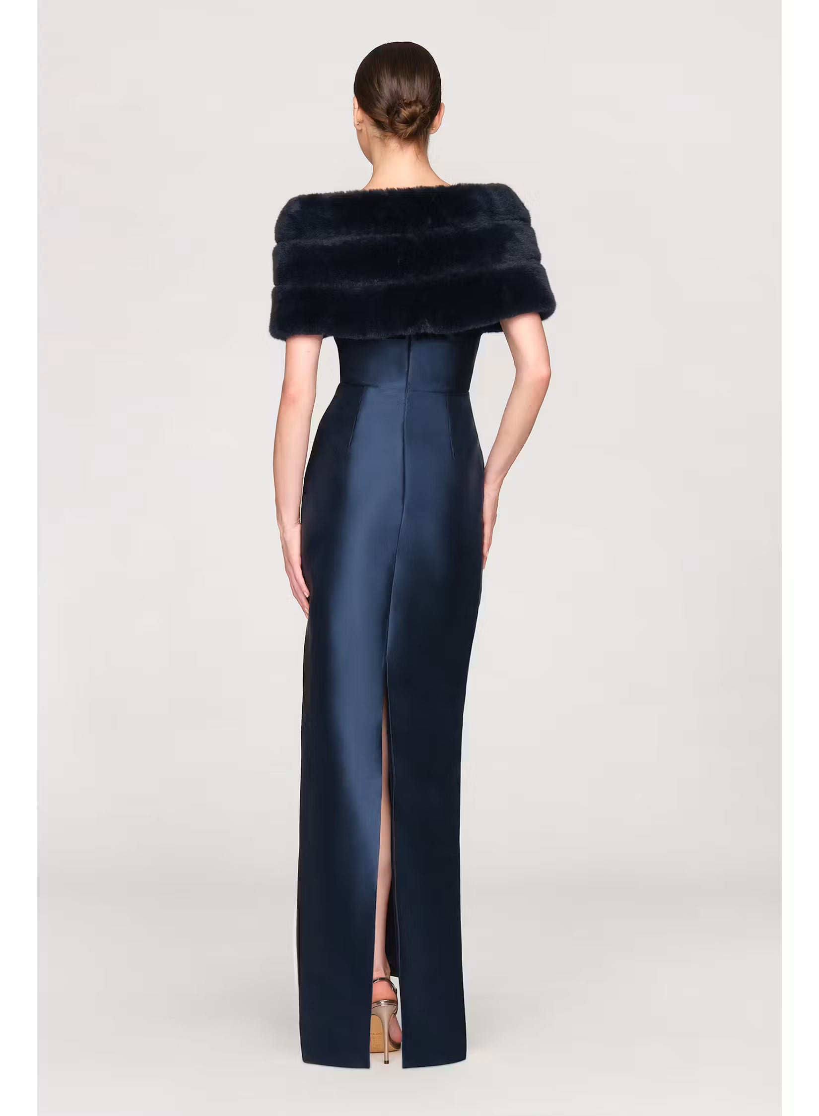 A woman is seen from the back, wearing a sleek navy gown with a high slit and a luxurious faux mink shawl draped over her shoulders.