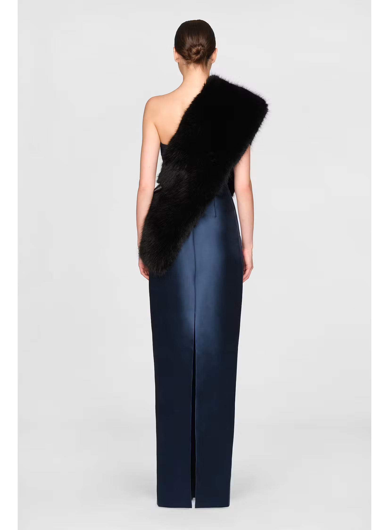 A model is showcasing a stunning black faux fur stole draped over one shoulder, paired with a sleek, high-waisted navy gown featuring a side slit.