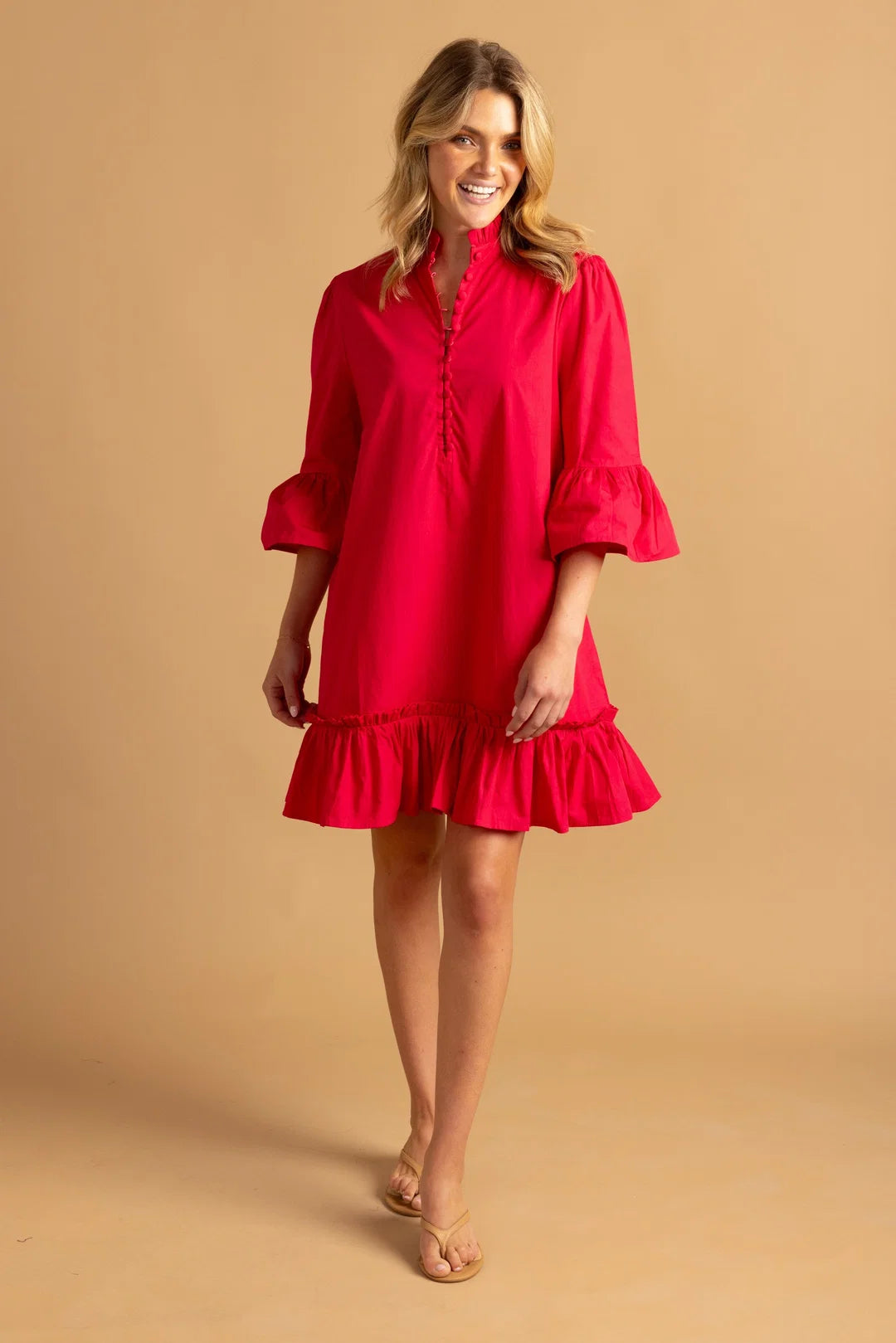 A woman stands confidently in a bright rose mini dress with a ruffled hem and flounce sleeves, showcasing a high neckline.