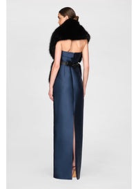 A woman stands gracefully in a sleek navy gown with a high slit, showcasing a stylish black faux fur stole draped elegantly over her shoulders. This sophisticated look is perfect for formal events like gala dinners or black tie weddings.