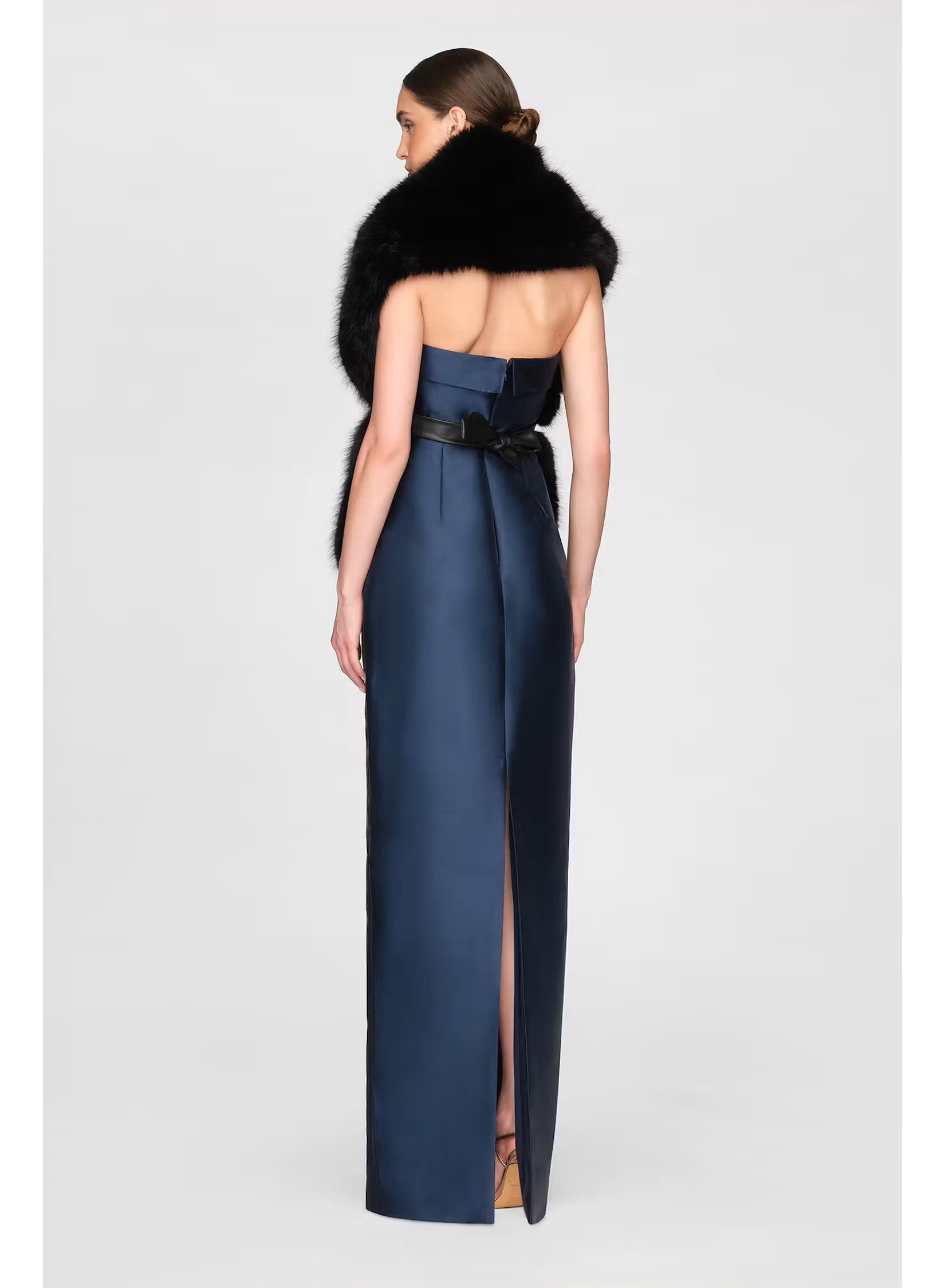 A woman stands gracefully in a sleek navy gown with a high slit, showcasing a stylish black faux fur stole draped elegantly over her shoulders. This sophisticated look is perfect for formal events like gala dinners or black tie weddings.
