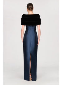A woman is wearing a fitted navy gown with a high slit and a luxurious black faux mink shawl draped over her shoulders.
