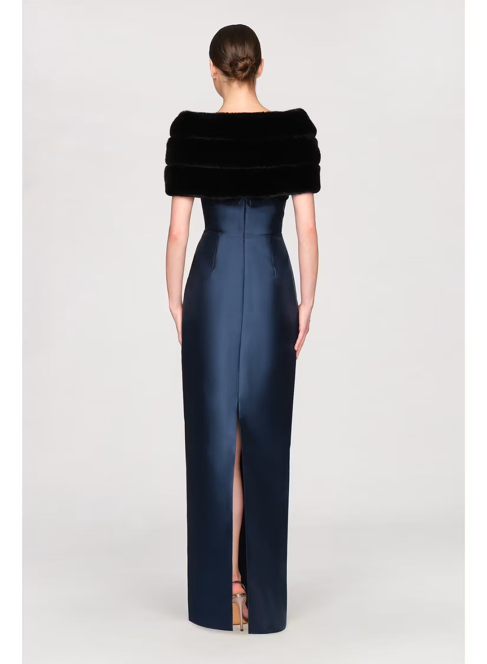 A woman is wearing a fitted navy gown with a high slit and a luxurious black faux mink shawl draped over her shoulders.